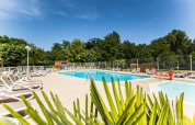 Outdoor swimming pool with sun loungers, lush trees, and blue sky at La Digue campsite in France.