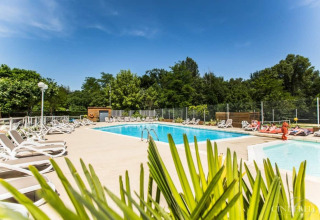 Udendørs swimmingpool med liggestole, grønne træer i baggrunden og klar blå himmel på La Digue campingplads.