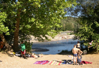 Campeggiatori si godono il sole e il fiume alberato al campeggio La Digue, parco vacanze in Francia.