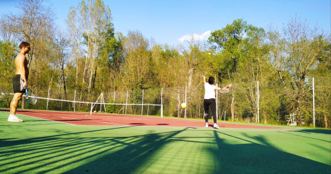 Due persone giocano a tennis su un campo all'aperto circondato da alberi al campeggio La Digue in Francia.