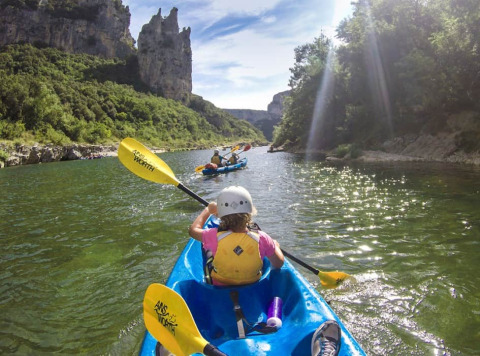 Persone in kayak sul fiume al campeggio La Digue in Auvergne-Rhône-Alpes, circondati da natura e scogliere.