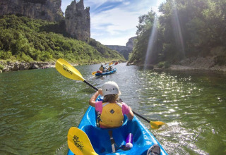 Persone in kayak sul fiume al campeggio La Digue in Auvergne-Rhône-Alpes, circondati da natura e scogliere.