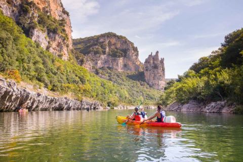 Persone fanno kayak su un fiume tranquillo vicino a Ruoms, circondato da alte scogliere verdi in Francia.