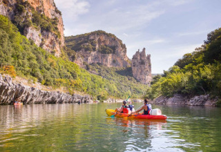 Persone fanno kayak su un fiume tranquillo vicino a Ruoms, circondato da alte scogliere verdi in Francia.