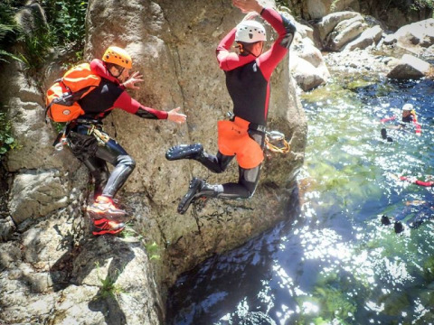 Due persone in mute e caschi saltano dalle rocce in acqua al campeggio La Digue, Auvergne-Rhône-Alpes, Francia.