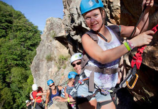 Un gruppo di persone scala una parete rocciosa con caschi e imbragature al campeggio La Digue, Francia.