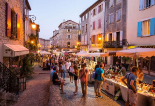 Vivace mercato serale nelle strade di Ruoms, Francia, con bancarelle illuminate e folla passeggiando.