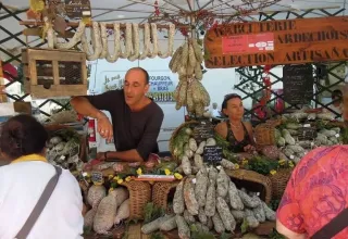 Scena di mercato vicino a Ruoms, Francia, con venditori locali e una vasta esposizione di salumi artigianali.