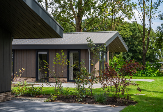 Moderne lodge Villa Veldzicht med træbeklædning, store vinduer og flot grøn have på en solskinsdag.