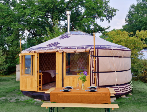 Mongoolse panorama-yurt met houten deur en buiten-eettafel, omringd door weelderig groen.