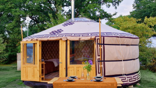 Mongoolse panorama-yurt met houten deur en buiten-eettafel, omringd door weelderig groen.