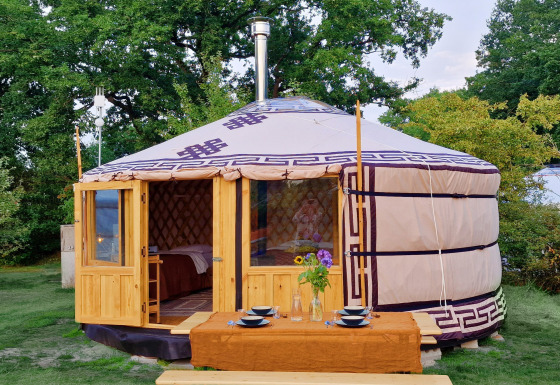 Mongoolse panorama-yurt met houten deur en buiten-eettafel, omringd door weelderig groen.