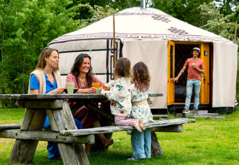 Familie zit rond een picknicktafel bij een Mongoolse yurt aan Mongolian Panorama Yurt in Zomerlicht, Nederland.