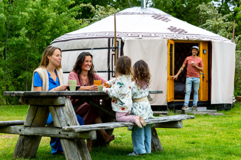 Familie zit rond een picknicktafel bij een Mongoolse yurt aan Mongolian Panorama Yurt in Zomerlicht, Nederland.