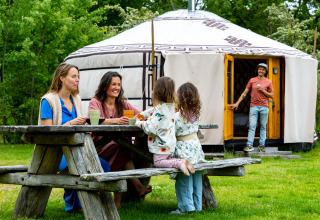Familie zit rond een picknicktafel bij een Mongoolse yurt aan Mongolian Panorama Yurt in Zomerlicht, Nederland.