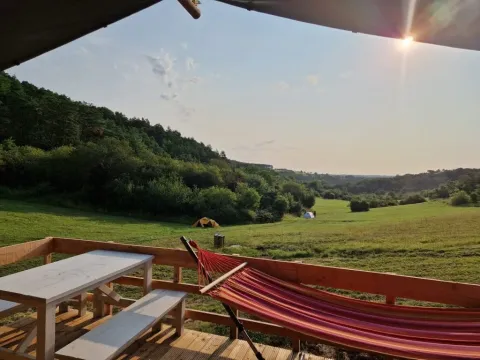 Vista da una terrazza a Les Terrasses de Dordogne con amaca, panche e tende su un prato soleggiato.