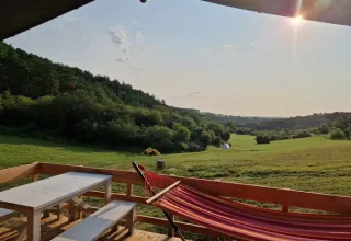 Vista da una terrazza a Les Terrasses de Dordogne con amaca, panche e tende su un prato soleggiato.