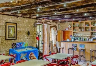 Foto dell'interno di un bar rustico con muri in pietra e travi in legno al campeggio Les Terrasses de Dordogne, Francia.
