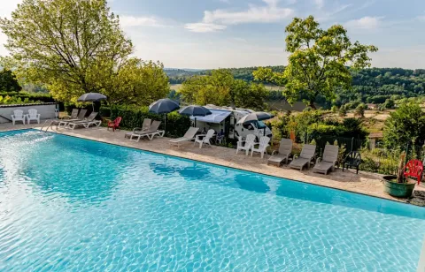 Piscina all'aperto con lettini e ombrelloni, vista sulle colline a Les Terrasses de Dordogne, Francia.