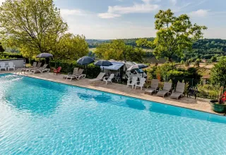 Piscine extérieure avec transats et parasols, vue sur les collines aux Terrasses de Dordogne, en France.
