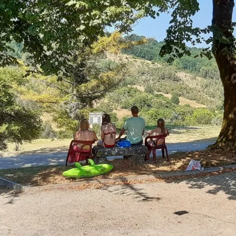 Una famiglia siede su sedie all’ombra di un albero godendosi la vista collinare in Dordogna.