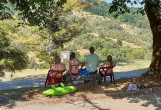 Una famiglia siede su sedie all’ombra di un albero godendosi la vista collinare in Dordogna.