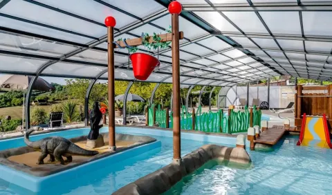 Piscina coperta al campeggio Les Terrasses de Dordogne con scivolo e dinosauro, area giochi in Francia.