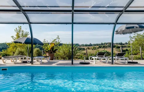 Piscina coperta con lettini e ombrelloni, vista sulle colline verdi alle Terrasses de Dordogne in Francia.