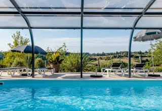Piscina coperta con lettini e ombrelloni, vista sulle colline verdi alle Terrasses de Dordogne in Francia.
