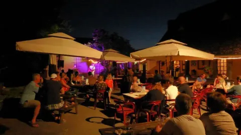 Atmosfera serale al campeggio Les Terrasses de Dordogne con ospiti che ascoltano musica dal vivo all’aperto.