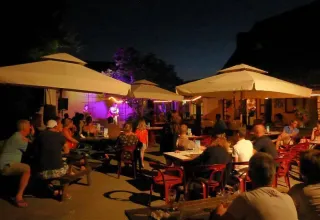 Atmosfera serale al campeggio Les Terrasses de Dordogne con ospiti che ascoltano musica dal vivo all’aperto.