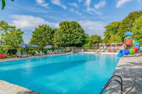 Piscina all'aperto con lettini, ombrelloni e scivolo colorato presso il campeggio Les Terrasses de Dordogne.