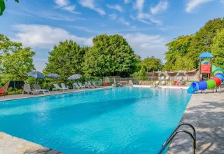 Piscina all'aperto con lettini, ombrelloni e scivolo colorato presso il campeggio Les Terrasses de Dordogne.