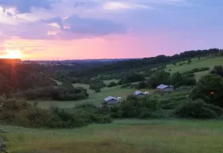Tramonto sulle colline verdi e le cabine al campeggio Les Terrasses de Dordogne, Nouvelle-Aquitaine, Francia.