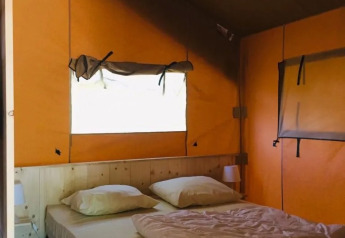 Vista interior de una tienda safari con cama doble, almohadas y luz natural entrando por la ventana.