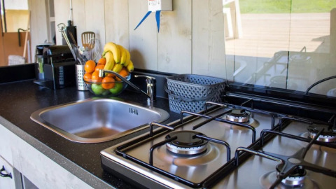 Cocina de tienda safari con fregadero, estufa de gas, frutero, utensilios y cestas en la encimera.