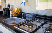Cocina de tienda safari con fregadero, estufa de gas, frutero, utensilios y cestas en la encimera.