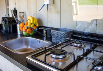 Cocina de tienda safari con fregadero, estufa de gas, frutero, utensilios y cestas en la encimera.
