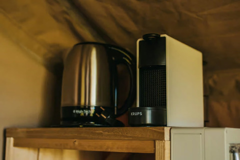 Ein Wasserkocher und eine Kaffeemaschine von Krups stehen auf einem Holzregal in einem Safarizelt.