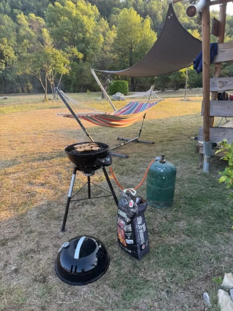 Área de barbacoa al aire libre junto a una tienda safari con hamaca, parrilla y bombona de gas en el césped.