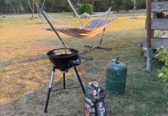 Área de barbacoa al aire libre junto a una tienda safari con hamaca, parrilla y bombona de gas en el césped.
