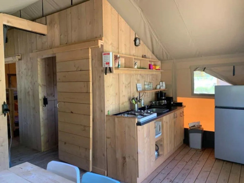 Interior de una tienda safari con paredes de madera, cocina pequeña, nevera y mesa de comedor iluminada.