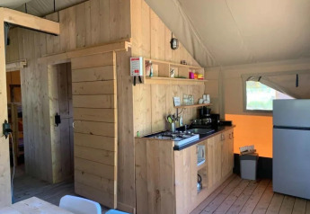Interior de una tienda safari con paredes de madera, cocina pequeña, nevera y mesa de comedor iluminada.