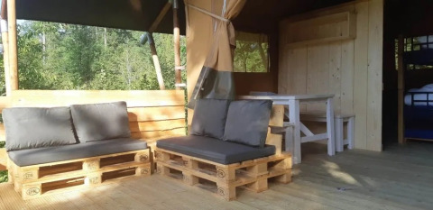 Zona de estar exterior en tienda safari con sofás de palets, cojines grises y mesa de madera.
