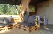 Gemütlicher Wohnbereich eines Safarizeltes mit Palettenmöbeln und Holzmöbeln im Grünen.