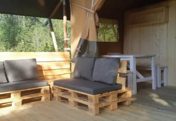 Zona de estar exterior en tienda safari con sofás de palets, cojines grises y mesa de madera.