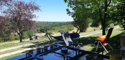 Vue depuis une tente safari avec salle de bain au camping Les Terrasses de Dordogne, champs et tracteur.
