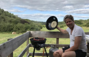 Man grilt worsten op terras met uitzicht op veld bij Safaritent met badkamer, Les Terrasses de Dordogne.