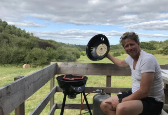 Homme faisant griller des saucisses sur la terrasse avec vue champêtre à Safaritent met badkamer, Les Terrasses de Dordogne.