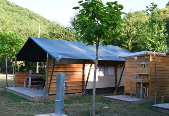 Safarizelt mit Holzterrasse und Außenbadezimmer, umgeben von grüner Natur und Bäumen.